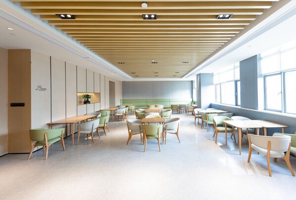 A modern interior with a high ceiling, recessed lighting, and a mix of seating arrangements including tables and chairs.