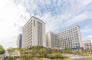 A modern hotel with multiple floors, large windows, and a well-maintained outdoor area with trees and a small pond. - Ji Hotel (Hangzhou)