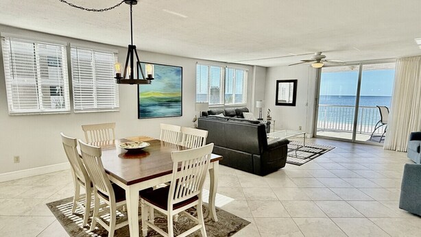 A spacious living area with a dining table, chairs, a sofa, and a balcony with a view of the ocean. - Spacious Beachfront Corner Condo in Madeira Beach| Gulf-Front|Pool & Hot-tub (Madeira Beach)