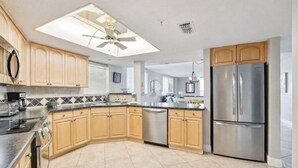 A modern kitchen with a skylight, a large refrigerator, and wooden cabinets. - Spacious Beachfront Corner Condo in Madeira Beach| Gulf-Front|Pool & Hot-tub (Madeira Beach)