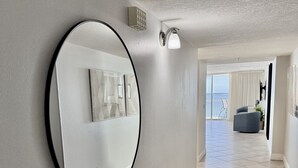A hallway with a large mirror, tiled floor, and a view of a balcony with a chair. - Spacious Beachfront Corner Condo in Madeira Beach| Gulf-Front|Pool & Hot-tub (Madeira Beach)