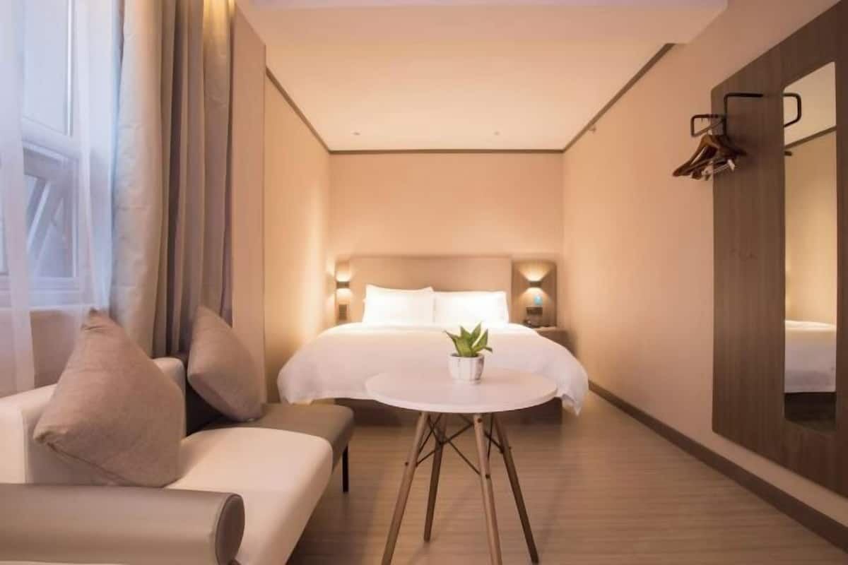 A modern hotel room with a large bed, a round table with a plant, and a sofa.