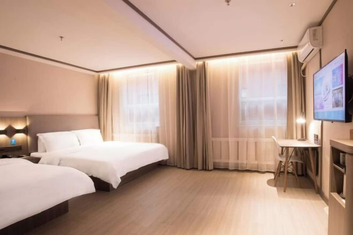 A hotel room with two beds, a desk, and a TV.