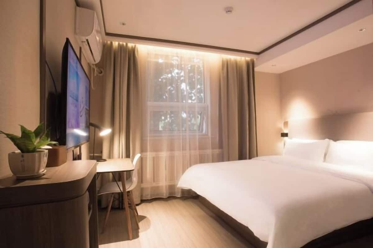 A hotel room with a bed, a desk, a chair, a television, and a window with curtains.