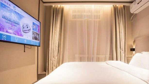 Ein Hotelzimmer mit einem großen Bett, einem an der Wand montierten Fernseher und einem Fenster mit durchsichtigen Vorhängen.