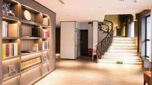 Eine Hotelhalle mit Holzboden, einer Treppe mit dekorativer Geländer und einem Bücherregal voller Bücher und Dekorationsgegenstände.