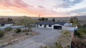 A modern two-story house with a garage, surrounded by a gravel driveway and sparse vegetation.