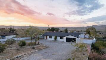 A modern two-story house with a garage, surrounded by a gravel driveway and sparse vegetation.