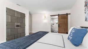 A bedroom with a bed, a blue patterned rug, a wooden wardrobe, and a bathroom visible through an open door.