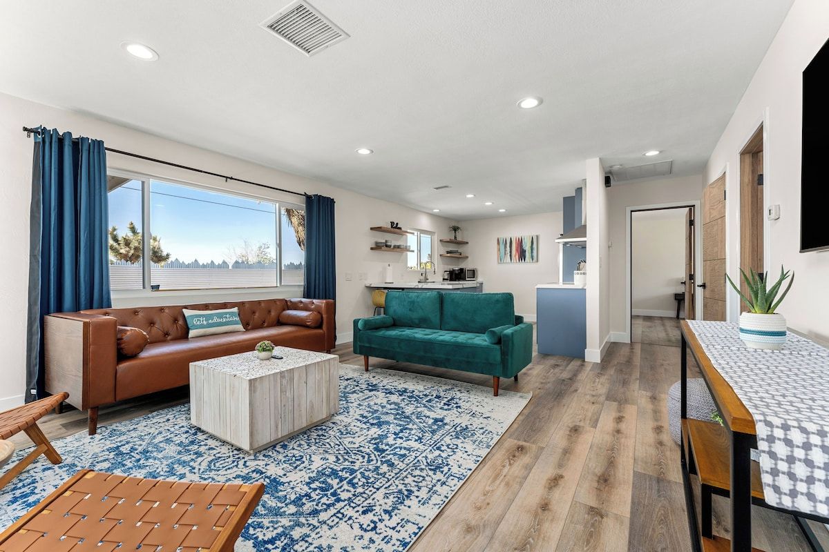 A modern living room with a brown leather sofa, a teal sofa, a coffee table, and a patterned rug.