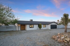 A single-story house with a garage, a gravel driveway, and a small tree.
