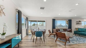 A spacious living area with a dining table, chairs, a sofa, and a large window offering a view of the outdoors.