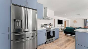 A modern kitchen with stainless steel appliances, a built-in oven, and a dining area with a green sofa.