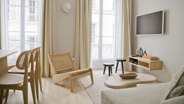 A modern living room with a sofa, wooden chairs, a small table, and a TV mounted on the wall. - Amazing Apt Prestige at Mouffetard Paris 5 (Paris)