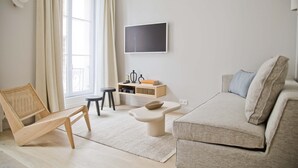 A modern living room with a sofa, a chair, a coffee table, a TV mounted on the wall, and a window with curtains. - Amazing Apt Prestige at Mouffetard Paris 5 (Paris)