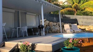 Ett takförsett utomhusområde med en pool, solstolar och krukväxter.