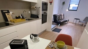 A modern kitchen with white cabinets, a toaster, a kettle, and a dining table set with yellow bowls and silverware. - Living PDL 1, new and contemporary apartment in the center of Ponta Delgada (Ponta Delgada)