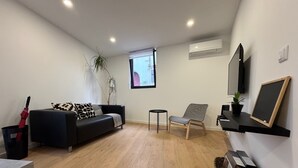 A modern living room with a black sofa, a grey armchair, a small table, and a TV mounted on the wall. - Living PDL 1, new and contemporary apartment in the center of Ponta Delgada (Ponta Delgada)
