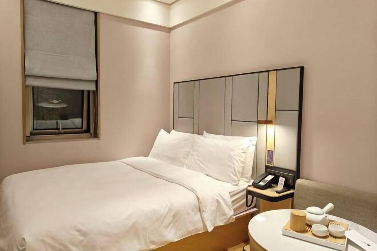 A neatly made bed with white linens, a bedside table with a lamp and a phone, and a round table with a tray of items.