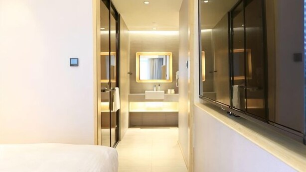 Un couloir d’hôtel avec un lit, une salle de bain dotée d’un lavabo et une grande fenêtre.