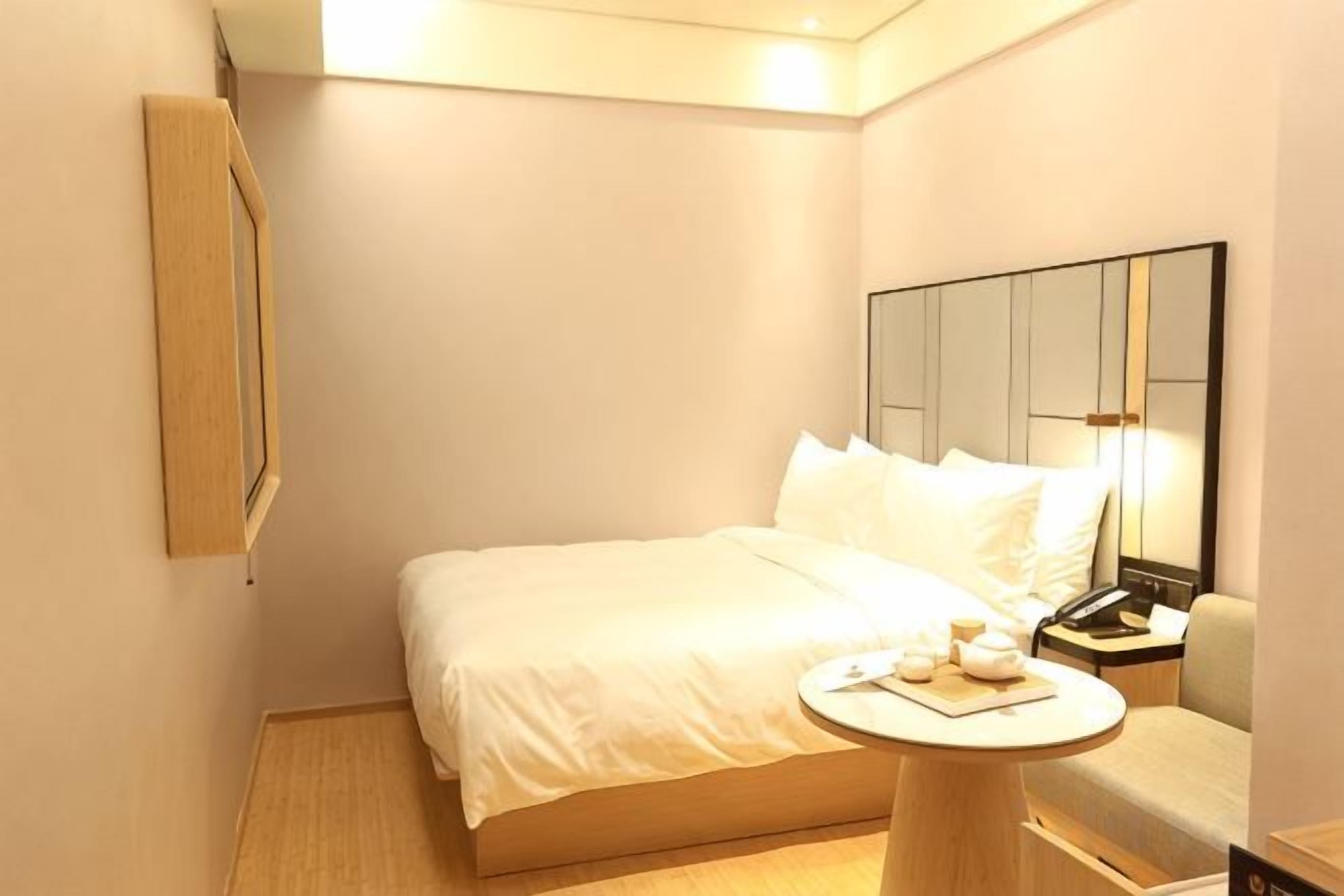 A hotel room with a bed, bedside table, lamp, and a mirror.