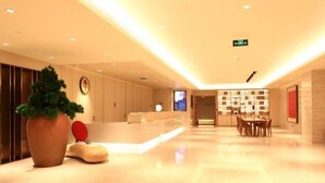 Un hall d’hôtel moderne avec un comptoir d’accueil, une grande plante en pot et un espace salon comprenant une table et des chaises.