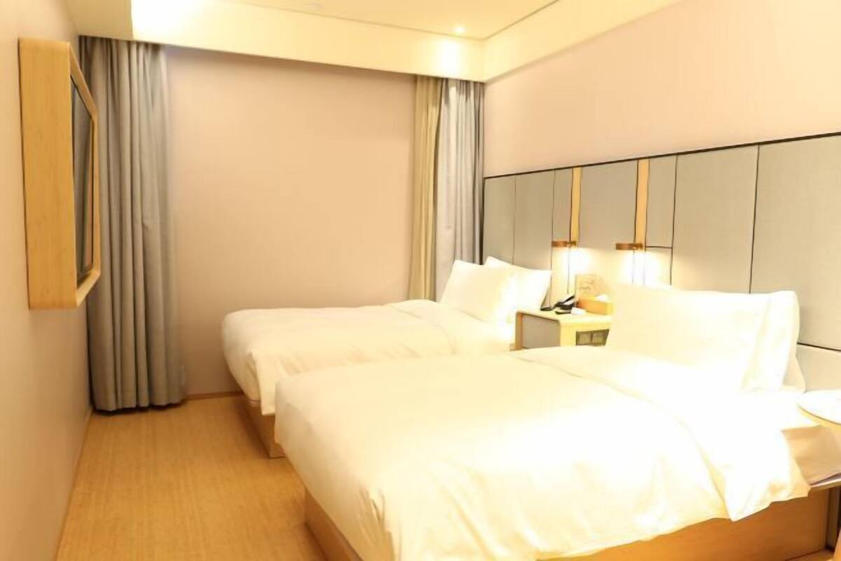 A hotel room with two beds, a large mirror, and a nightstand with a lamp.