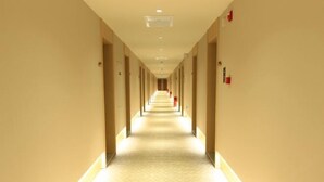 Un long couloir d’hôtel, bien éclairé, avec un tapis à motifs et des murs de couleur beige.
