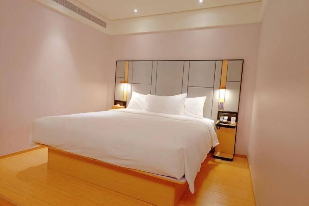 A modern hotel room with a large bed, wooden flooring, and a headboard with integrated lighting.