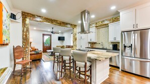 A modern kitchen with a central island, stainless steel appliances, and a dining area with bar stools. - Chic Louisiana Retreat - Balcony & River Views! (New Roads)
