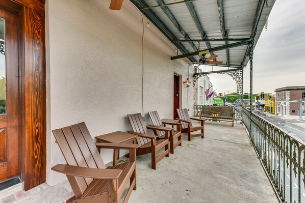 A covered outdoor seating area with wooden chairs and tables, a bench, and a view of the street.