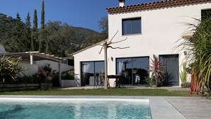 Et moderne hus med swimmingpool, terrasse med udendørs møbler og udsigt til et bakket landskab.