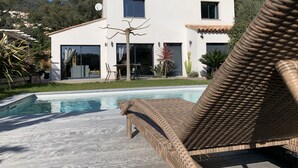 Et moderne hus med to etager, en swimmingpool, udendørs møbler og en have.