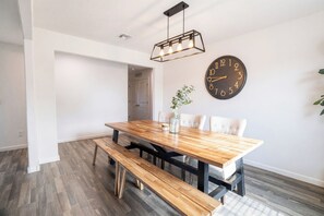 A dining area with a wooden table, benches, a wall clock, and a hanging light fixture. - 4BR Casa Grande Home | Fast WiFi, Grill + Sleeps 8 (Casa Grande)