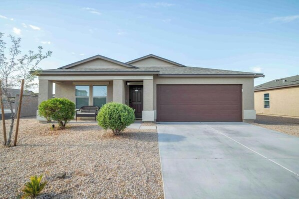 A single-story house with a garage, a front porch, and a gravel driveway. - 4BR Casa Grande Home | Fast WiFi, Grill + Sleeps 8 (Casa Grande)