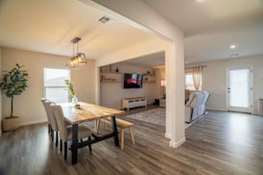 A modern living room with a dining area, a flat-screen TV, and a sofa.