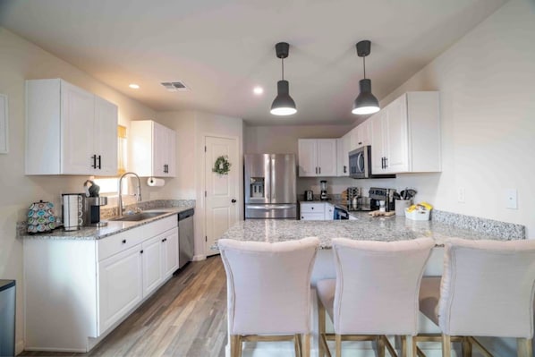 A modern kitchen with white cabinets, a granite countertop, stainless steel appliances, and pendant lighting.