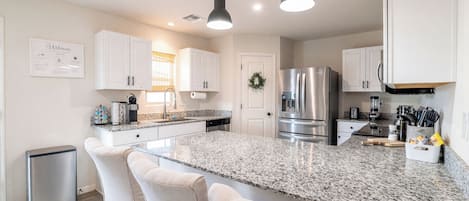 A modern kitchen with a central island, white cabinetry, stainless steel appliances, and pendant lighting.