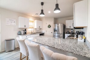 A modern kitchen with a central island, white cabinetry, stainless steel appliances, and pendant lighting. - 4BR Casa Grande Home | Fast WiFi, Grill + Sleeps 8 (Casa Grande)