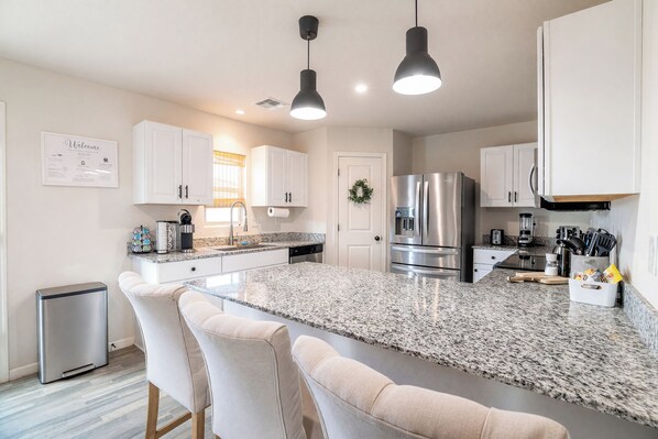 A modern kitchen with a central island, white cabinetry, stainless steel appliances, and pendant lighting.