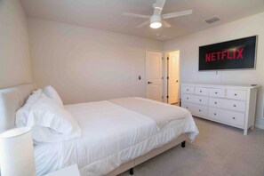 A bedroom with a bed, a dresser, a ceiling fan, and a wall-mounted television displaying 'NETFLIX'.