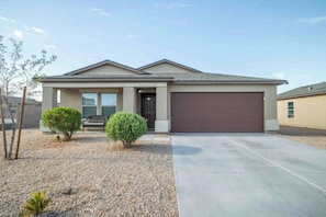 A single-story house with a front garage, a covered porch, and two small shrubs. - 4BR Casa Grande Home | Fast WiFi, Grill + Sleeps 8 (Casa Grande)