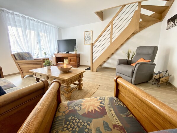 A living room with a wooden coffee table, a sofa, a TV, and a staircase. - Le Familik - Maison - Centreville (Licques)
