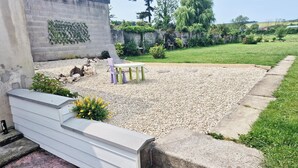 A gravel patio with a white wall, a concrete bench, and a small garden area with yellow flowers.