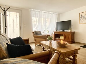 A living room with a wooden table, a television, and a sofa with cushions. - Le Familik - Maison - Centreville (Licques)