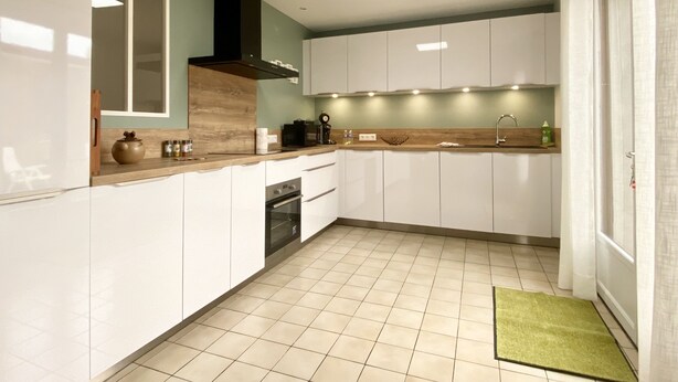A modern kitchen with white cabinets, a wooden countertop, and a tiled floor.