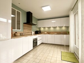 A modern kitchen with white cabinets, a wooden countertop, and a tiled floor. - Le Familik - Maison - Centreville (Licques)