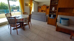 A dining area with a table and chairs, a sofa, and a bookshelf. - Fréjus Plage, Le Sextant, Large T2 of 52m2, 3/4 people, swimming pool, large balcony, WIFIair-conditioned living room, 400m from the beach (Fréjus)