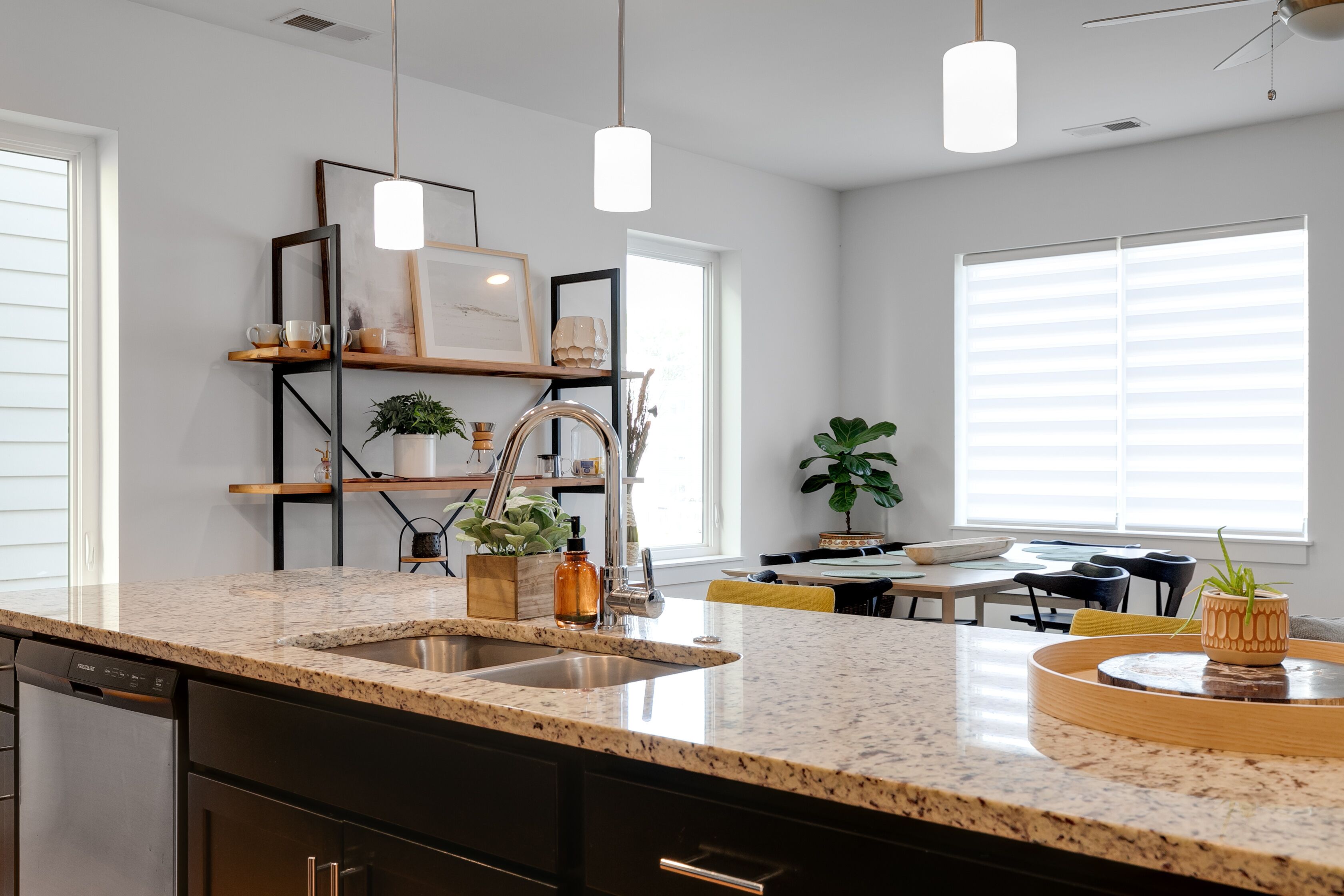 A modern kitchen with granite countertops, a built-in dishwasher, and a dining area with a yellow chair and a table.