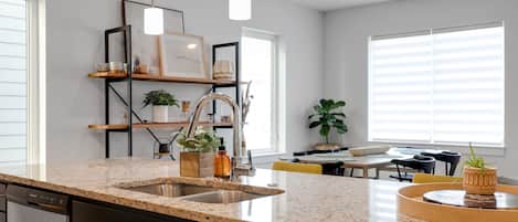 A modern kitchen with granite countertops, a built-in dishwasher, and a dining area with a yellow chair and a table.